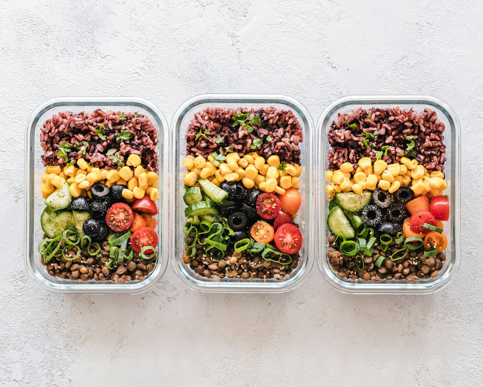Three glass containers filled with rice, corn, olives, tomatoes, cucumbers, and lentils