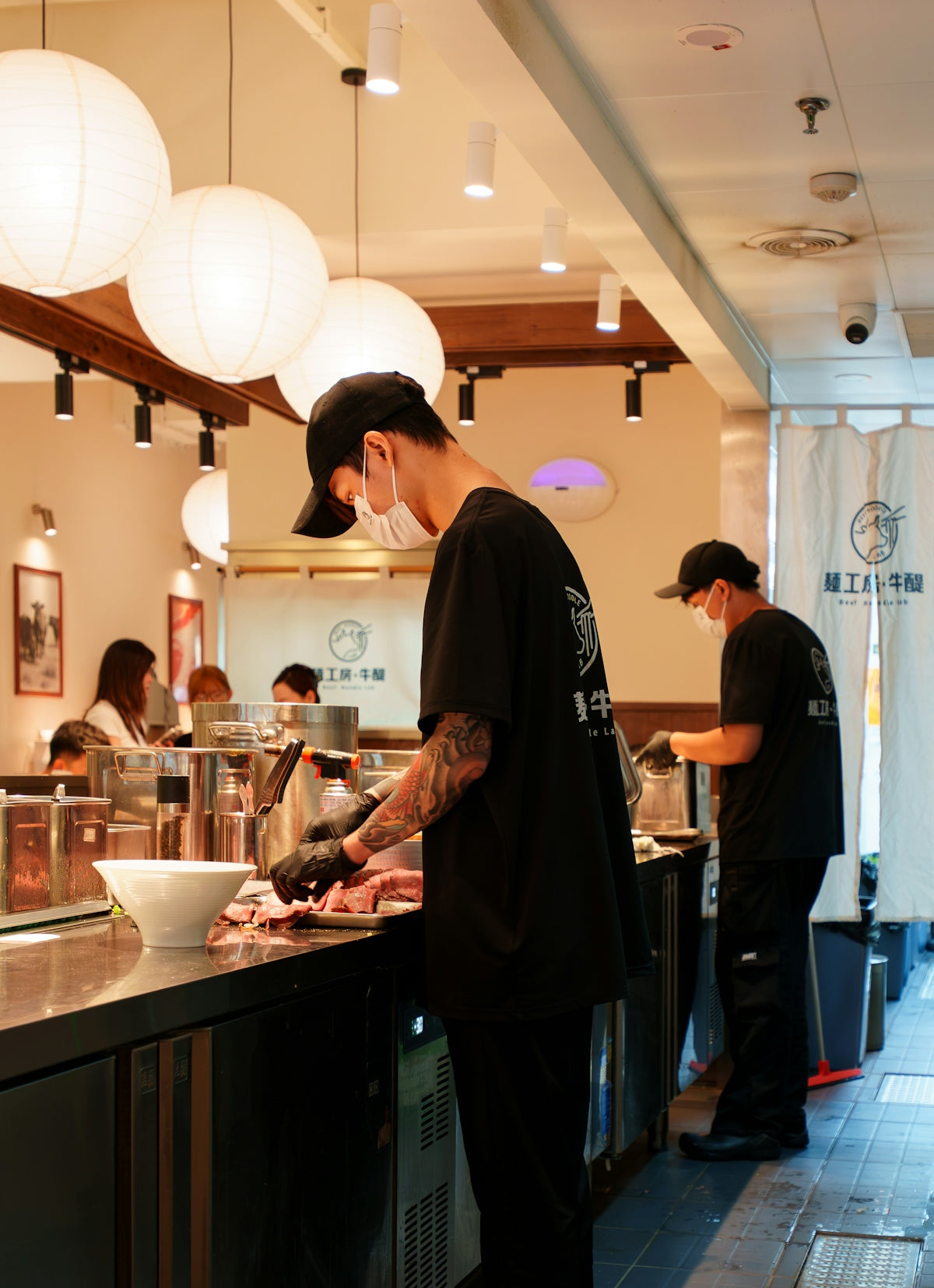 Two chefs in black uniforms preparing meat in a restaurant kitchen