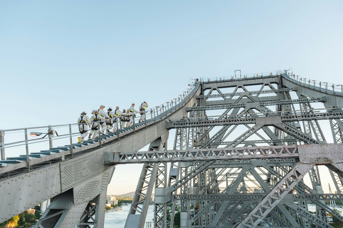 A group of people in safety harnesses climbing the steel structure of a bridge